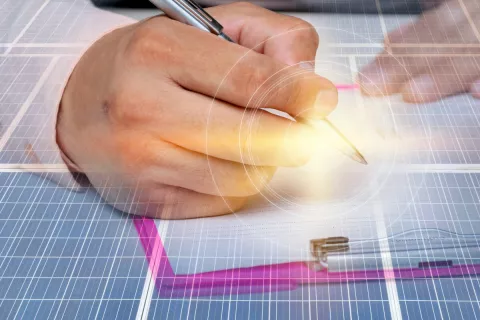 Eine Hand unterschreibt die Registrierung einer PV-Anlage, im Hintergrund liegt eine Solarpanel.